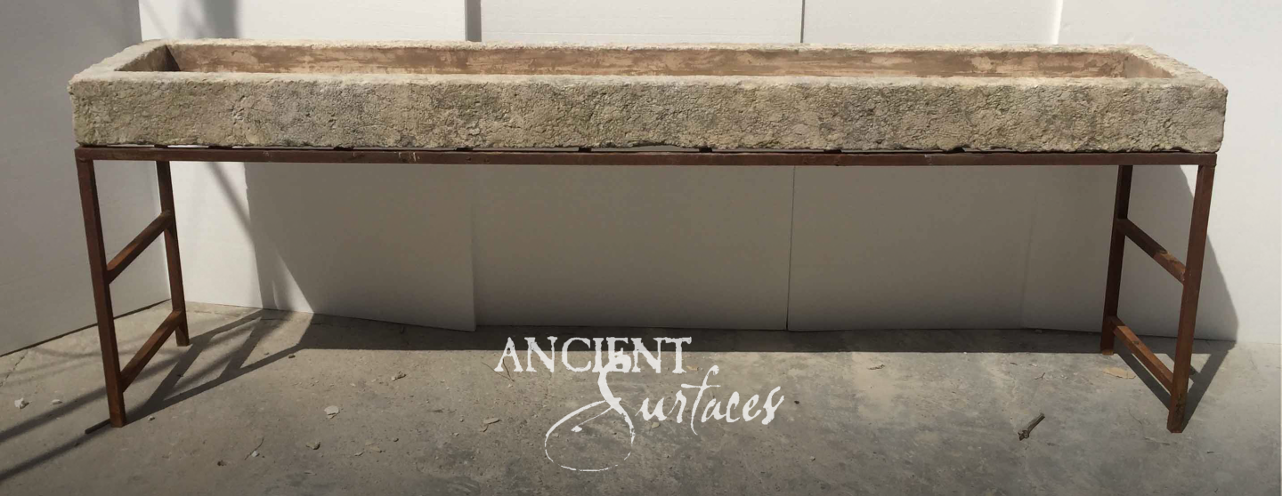 Elongated weathered tan stone trough on a rusted square-tube steel base